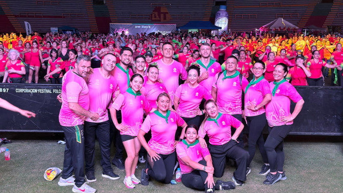 Grupo de instructores en camisetas rosadas posan frente a cientos de participantes en un estadio durante evento deportivo masivo.
