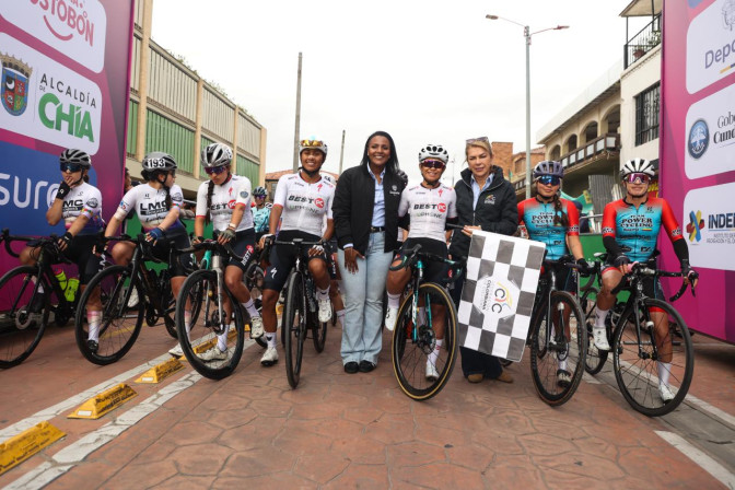 Ciclistas y autoridades posan en la línea de salida de la Vuelta a Colombia Femenina 2026 en Chía, sosteniendo una bandera a cuadros.