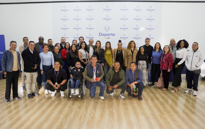 Grupo de aproximadamente 30 personas posando frente al telón institucional del Ministerio de Deporte de Colombia, incluyendo una persona en silla de ruedas.