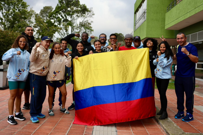 Grupo de deportistas y cuerpo técnico colombiano sostienen la bandera de Colombia con puños en alto en señal de orgullo y fortaleza.