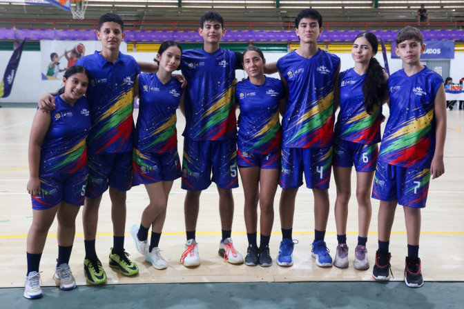 Ocho jóvenes deportistas con uniforme azul del INDER posan juntos en un coliseo durante los Juegos Intercolegiados 2025.