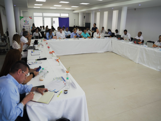 Numeroso grupo de funcionarios reunidos en mesa en U durante sesión institucional en Valledupar, con banners oficiales al fondo.