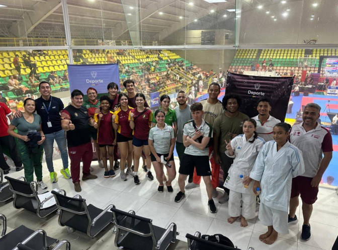 Grupo de atletas, entrenadores y personal de apoyo posando en un coliseo deportivo durante un evento de karate y artes marciales.