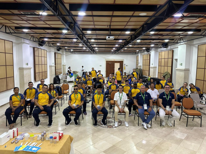 Grupo numeroso de deportistas y cuerpo técnico con uniformes amarillo y azul posando en salón de eventos durante reunión institucional.