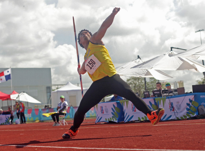 Atleta con dorsal 150 y camiseta amarilla ejecuta lanzamiento de jabalina en pista atlética durante evento deportivo internacional.